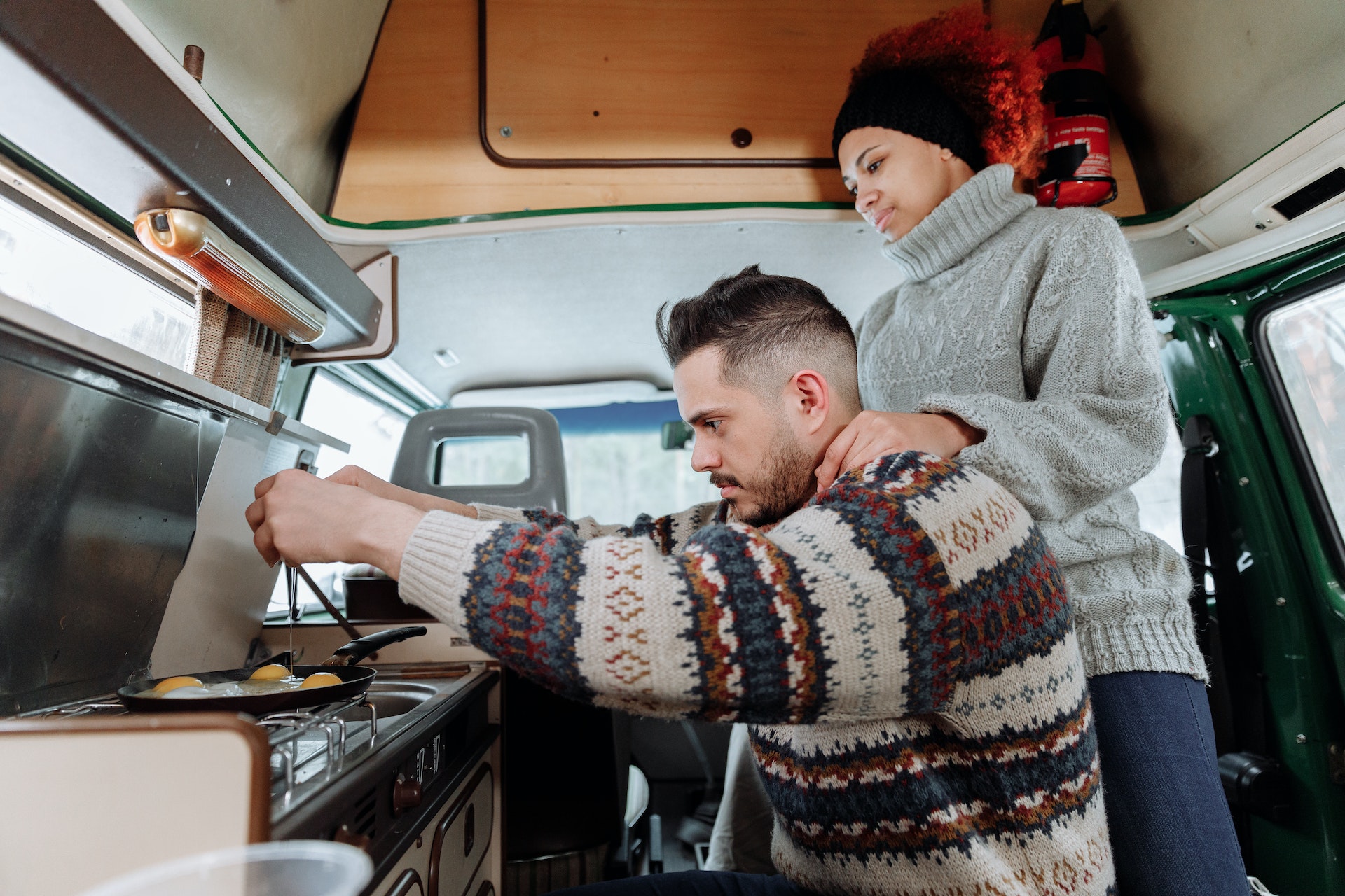 Man and woman cooking an egg on stove in camper